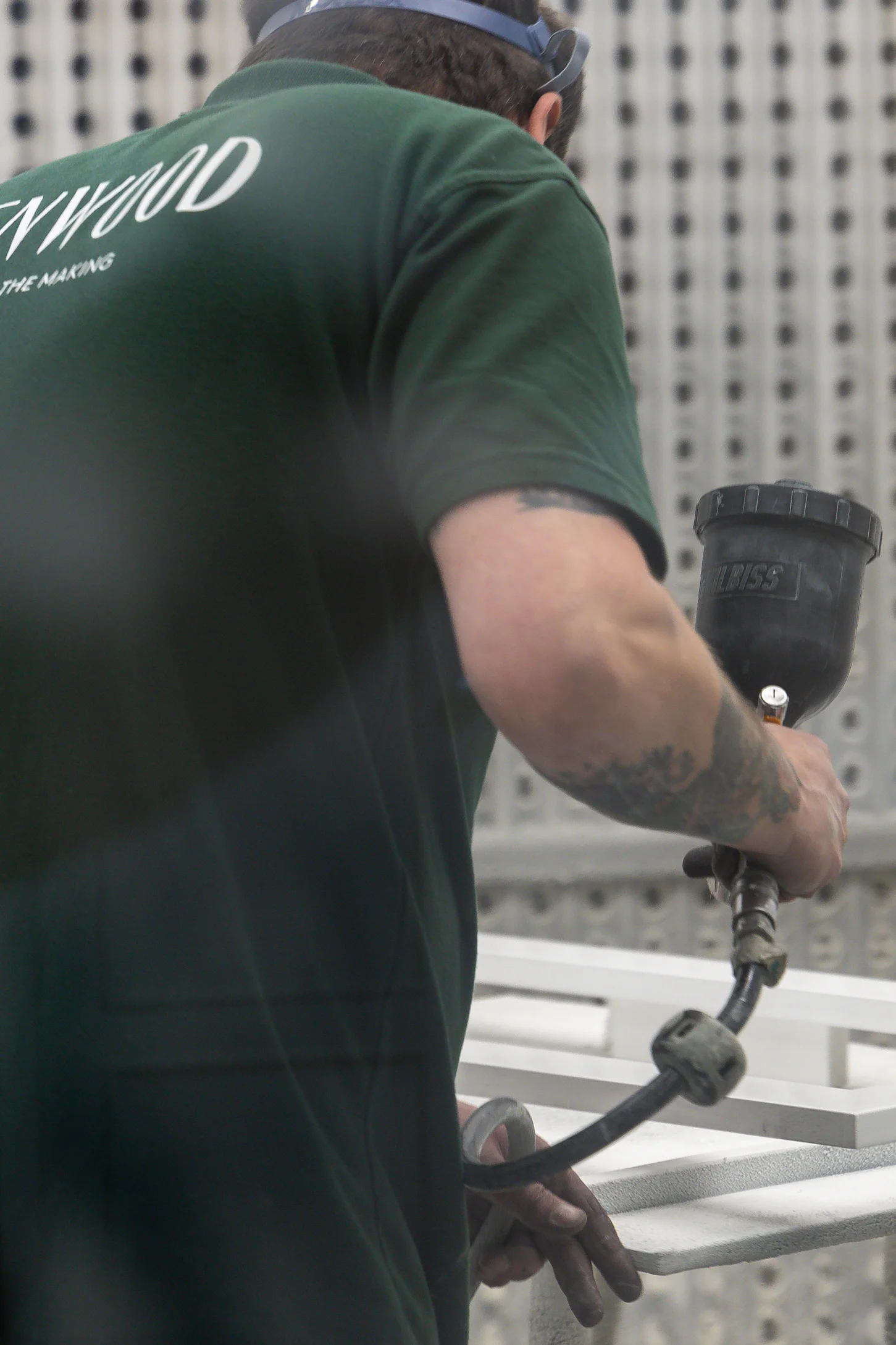 A man wearing a green shirt is applying paint to a white surface with a spray gun.