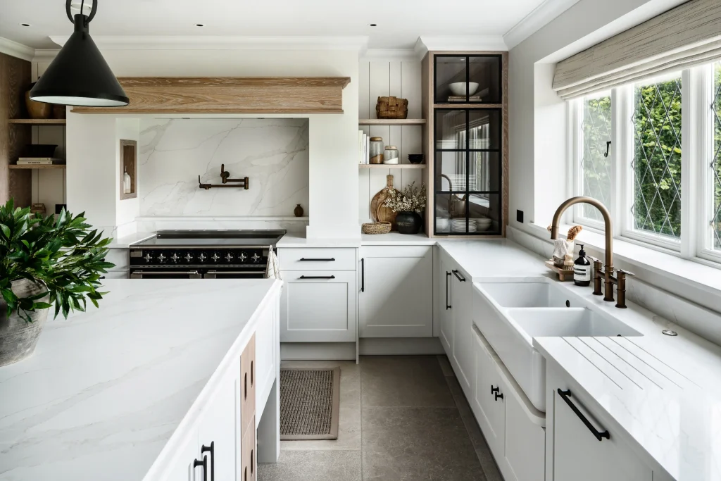 Bright modern kitchen with white marble countertops, farmhouse sink, brass faucet, black hardware, and window over sink.