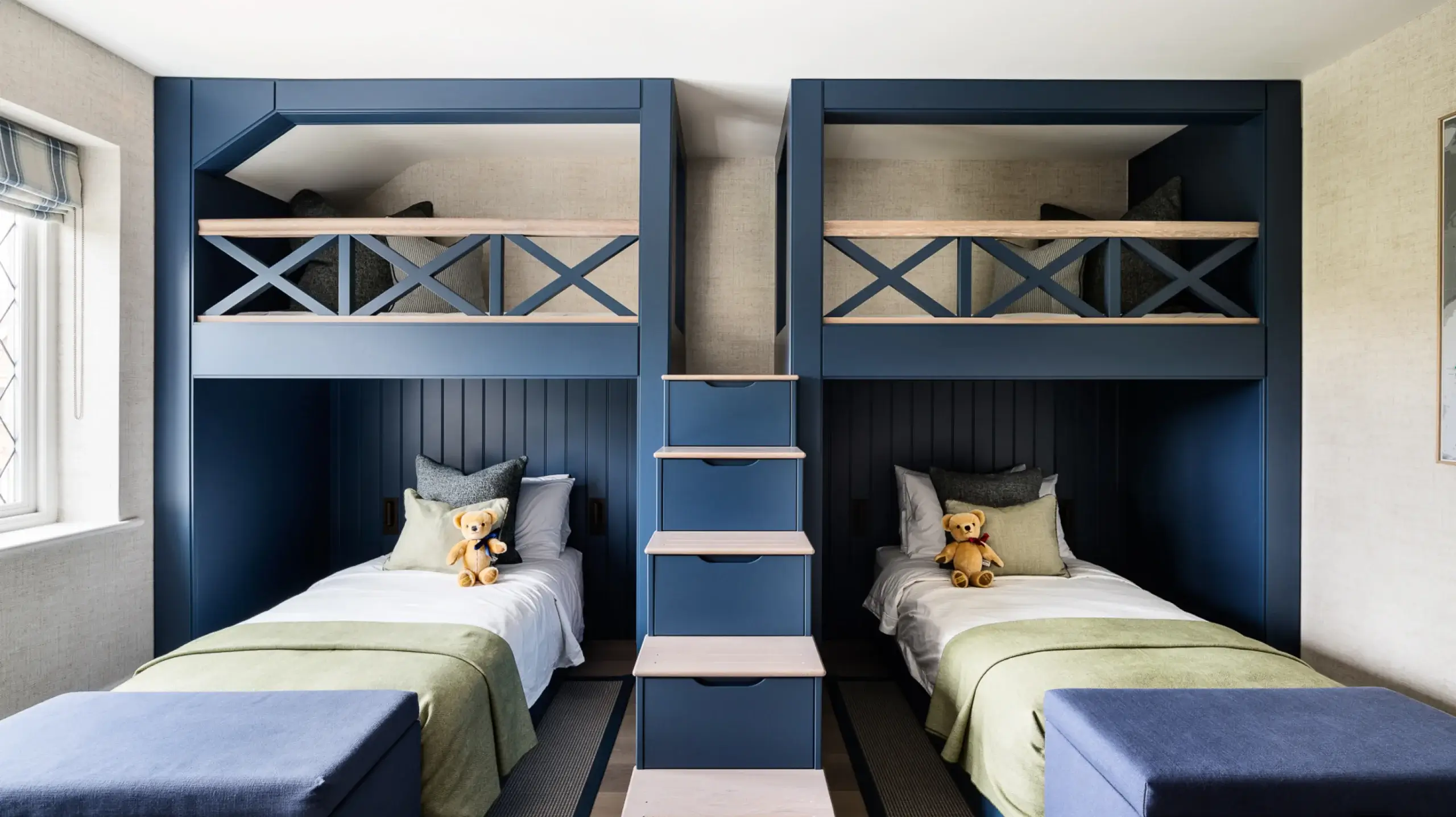 Symmetrical navy built-in bunk beds with central staircase, twin lower beds dressed in green throws and teddy bears on each pillow