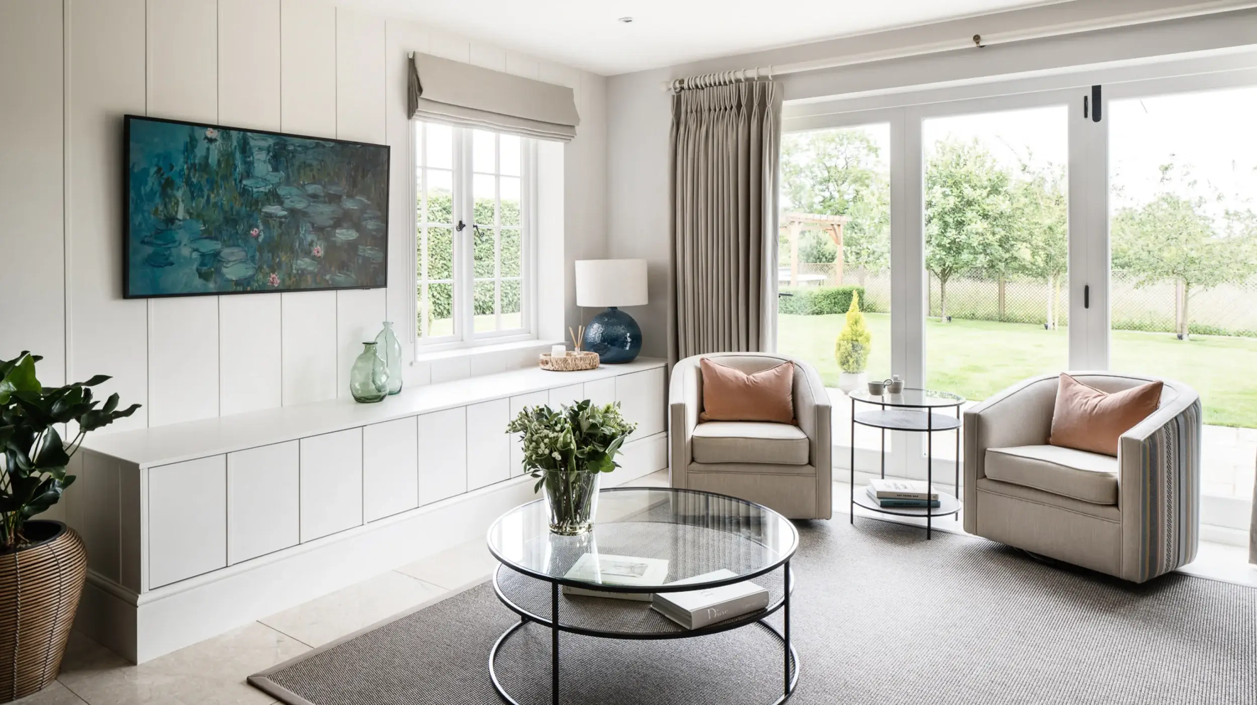 Living room with glass table and comfortable chair, with bespoke fitted cabinetry under the window