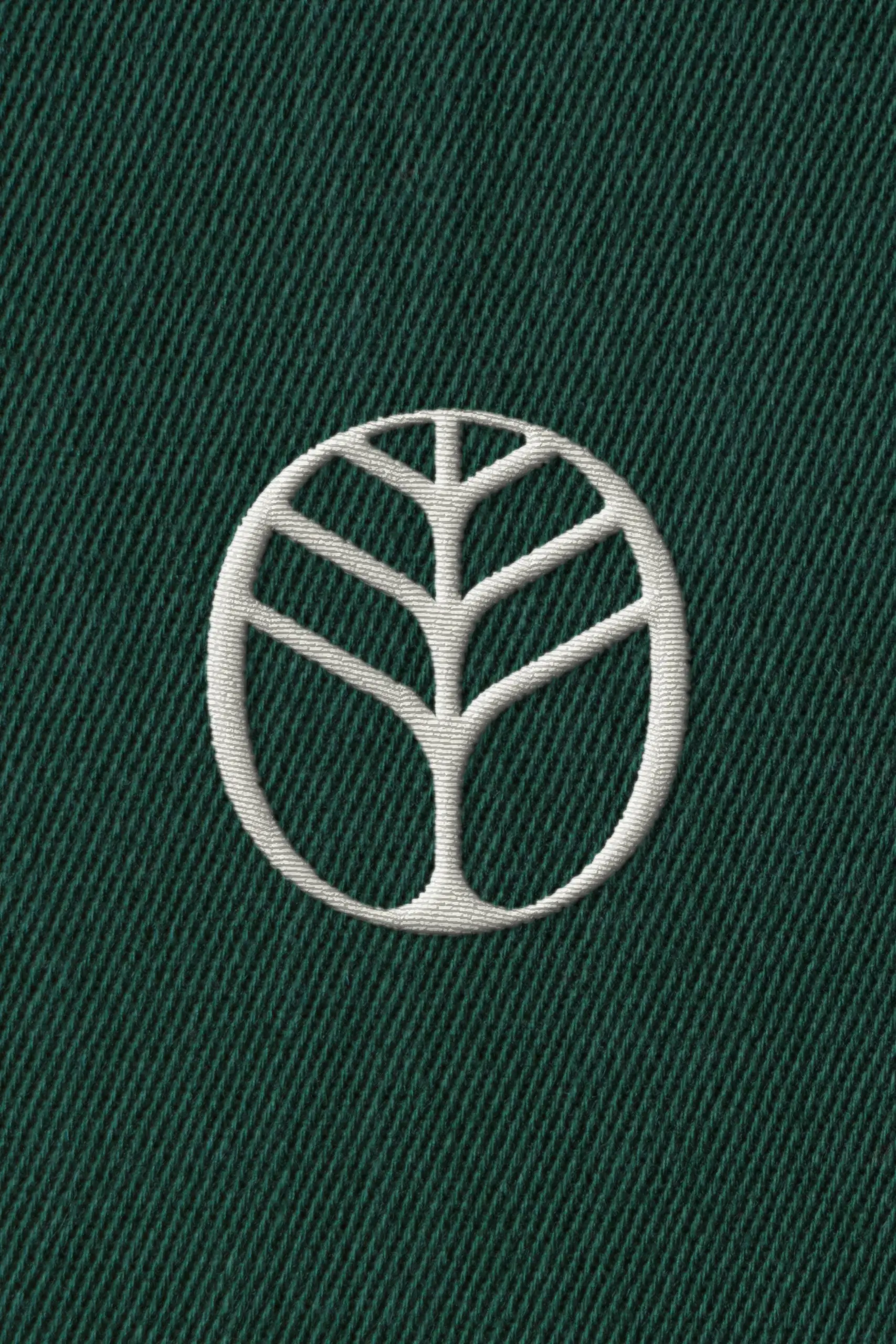 White embroidered circular tree logo with stylized branches on dark green diagonal twill fabric background.