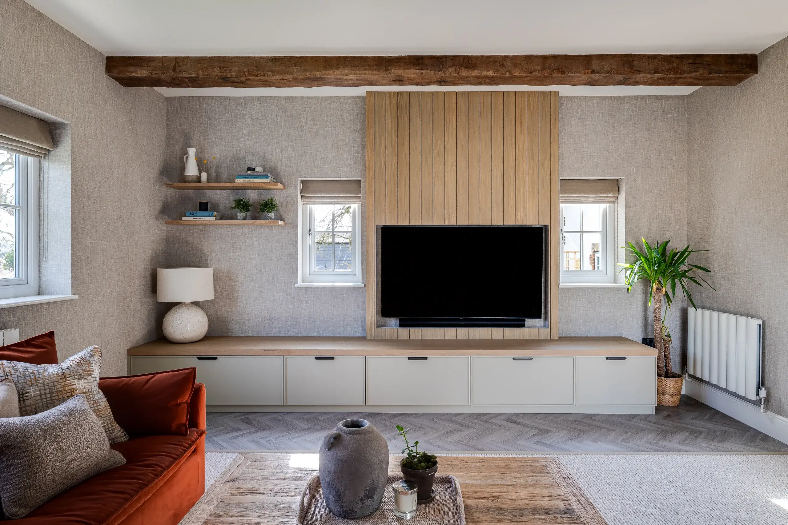 Living room with wall-mounted TV set in wood paneling, low storage cabinets, rust sofa, potted plant, and decorative shelves.