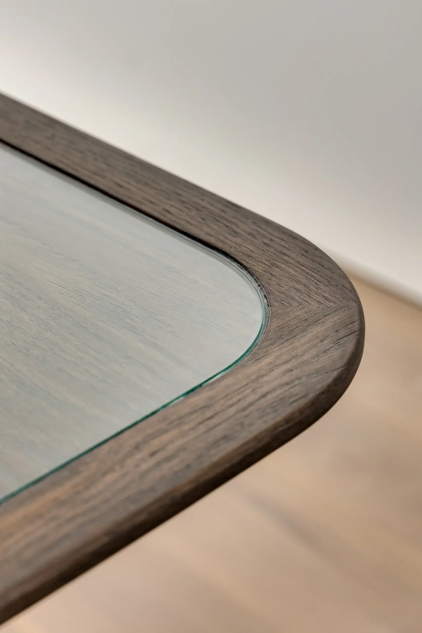 Close-up of a rounded wooden table corner with an inset glass top showing wood grain and beveled glass edge.