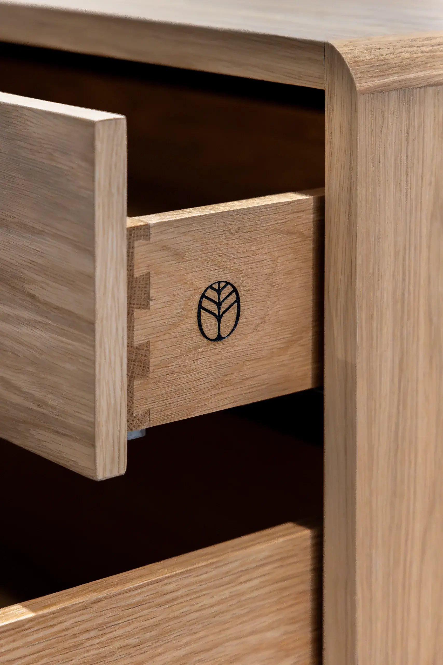 Close-up of a wooden drawer with dovetail joints and a small circular logo showing a stylized leaf inside.