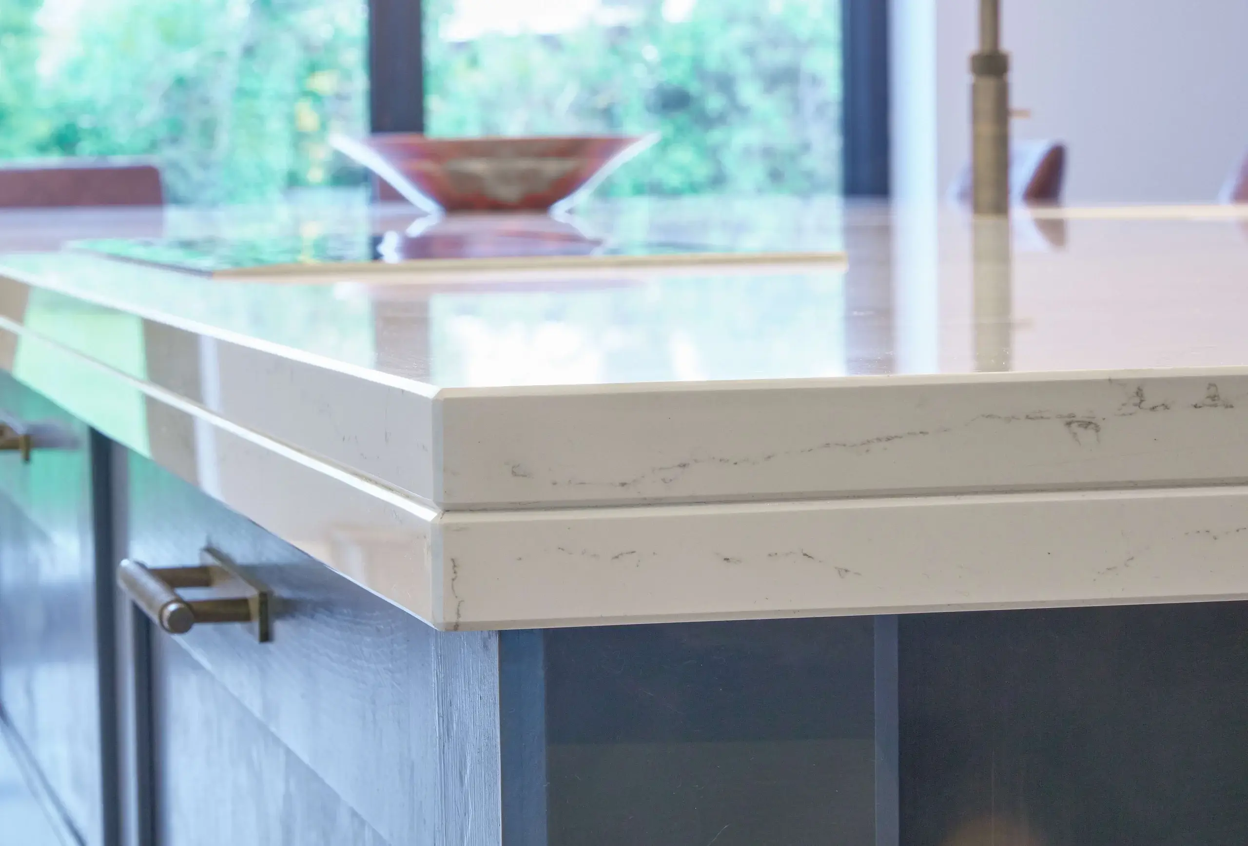 Close-up of a white marble kitchen island countertop with subtle gray veining and a dark cabinet base with metal handle.