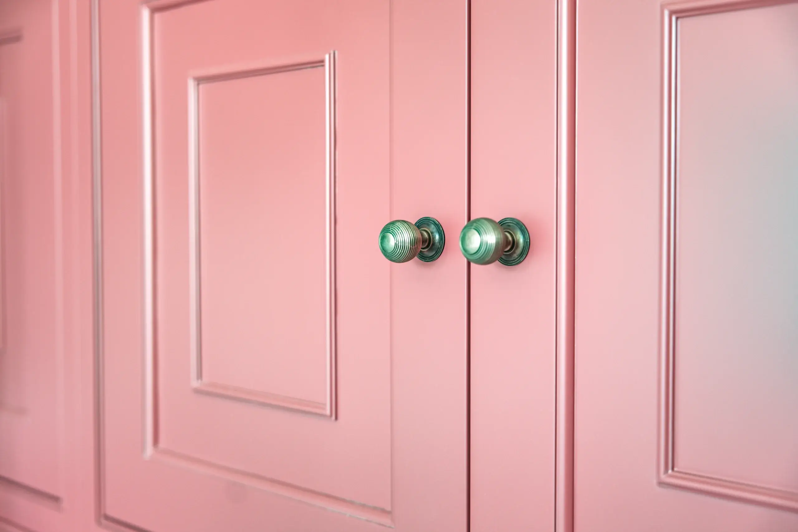 Pair of green glass knobs centered on pink paneled cabinet doors with raised rectangular molding