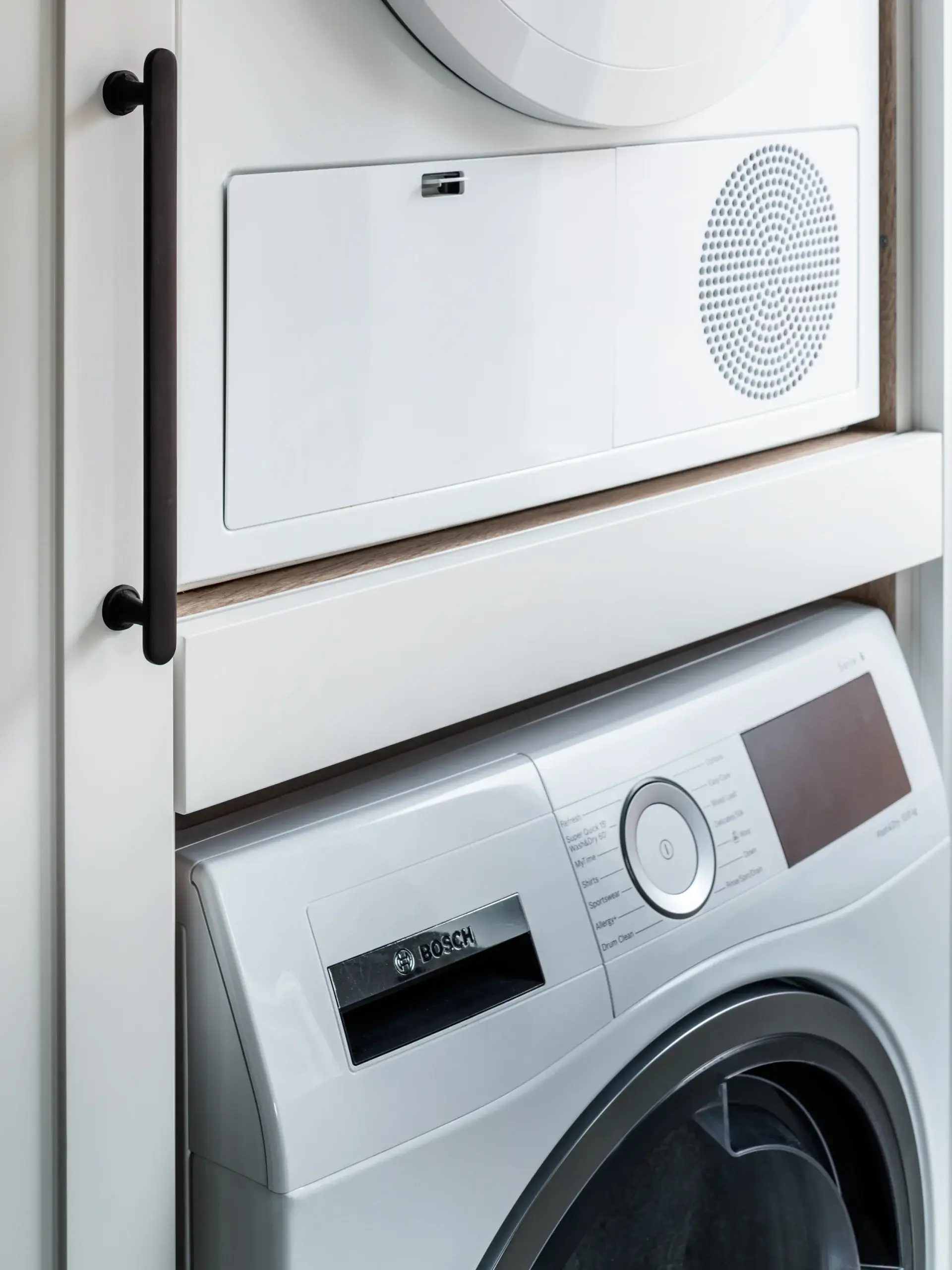 Stacked white front-loading washer and dryer in a closet with black vertical handle and Bosch washer control panel visible.