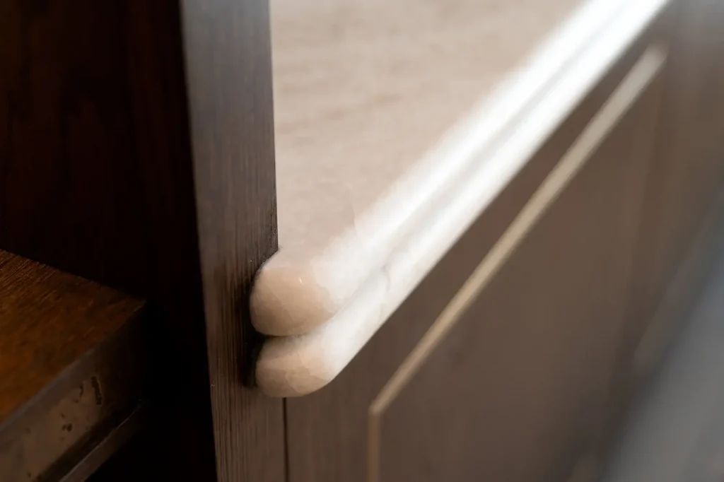 Close-up of a rounded white marble countertop edge meeting a dark wood cabinet panel with a decorative profile.