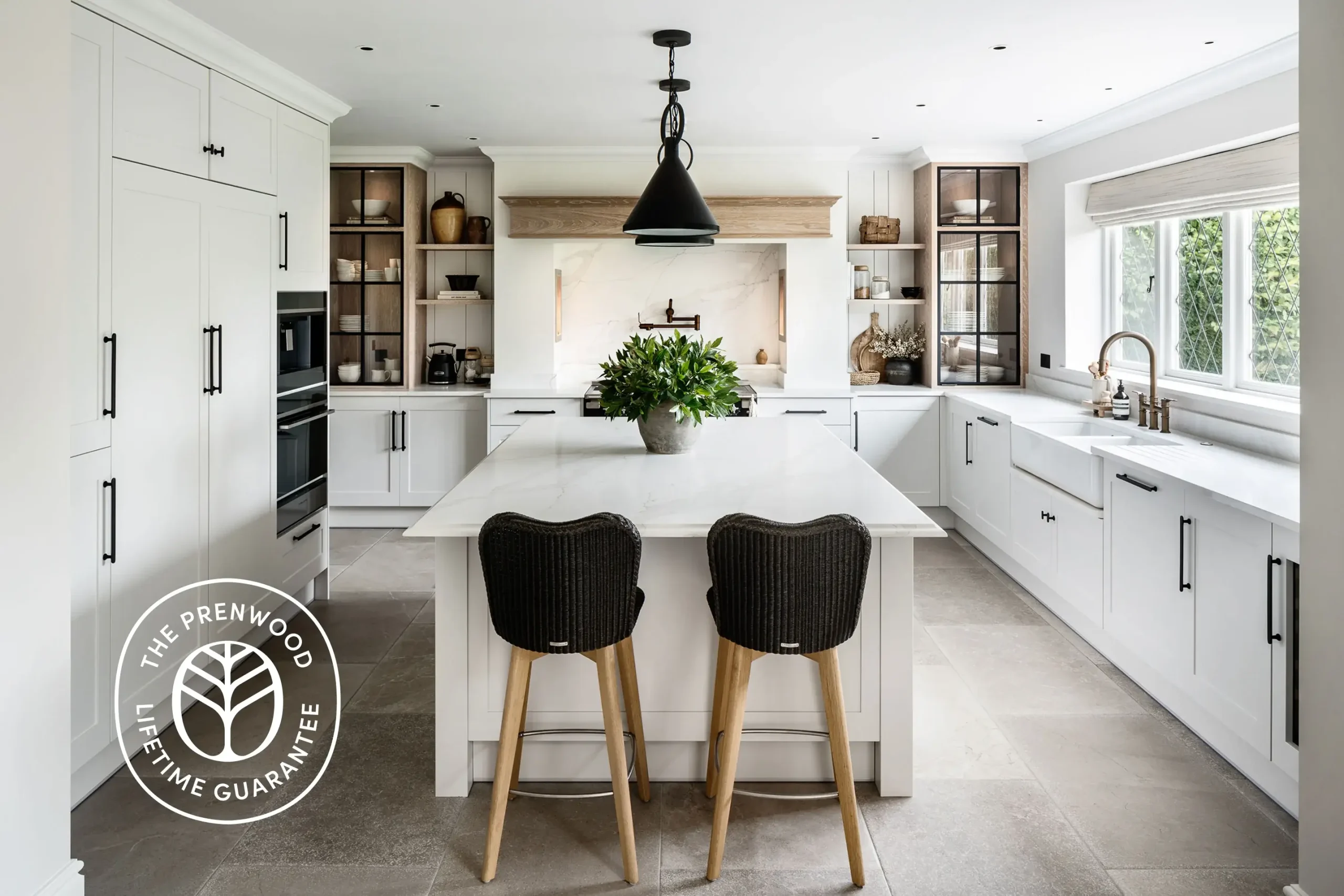 Bright modern white kitchen with large marble island, two wicker bar stools, pendant light, and potted plant centerpiece.