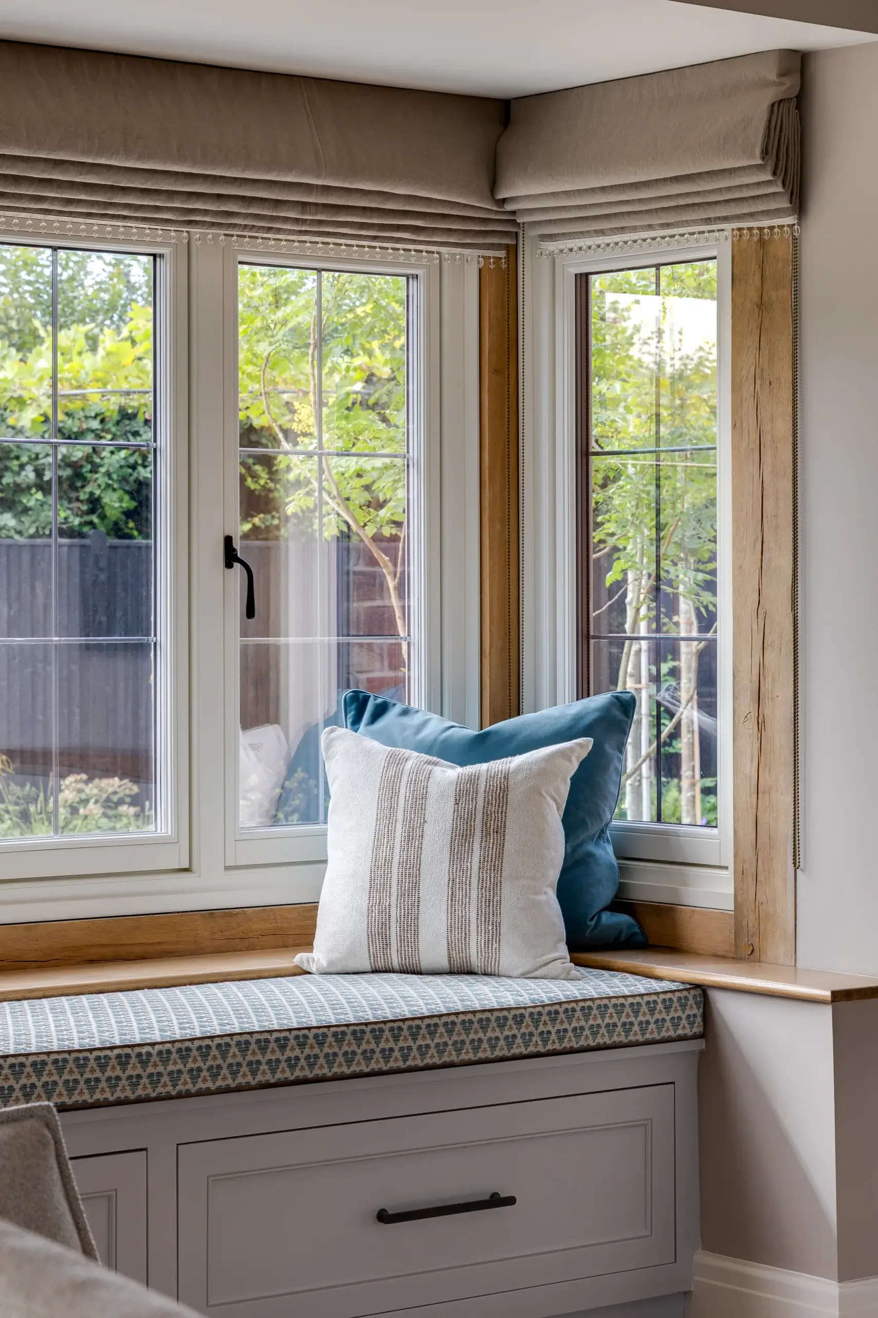 Window seat with patterned cushion and two throw pillows in front of three paneled windows showing green yard outside