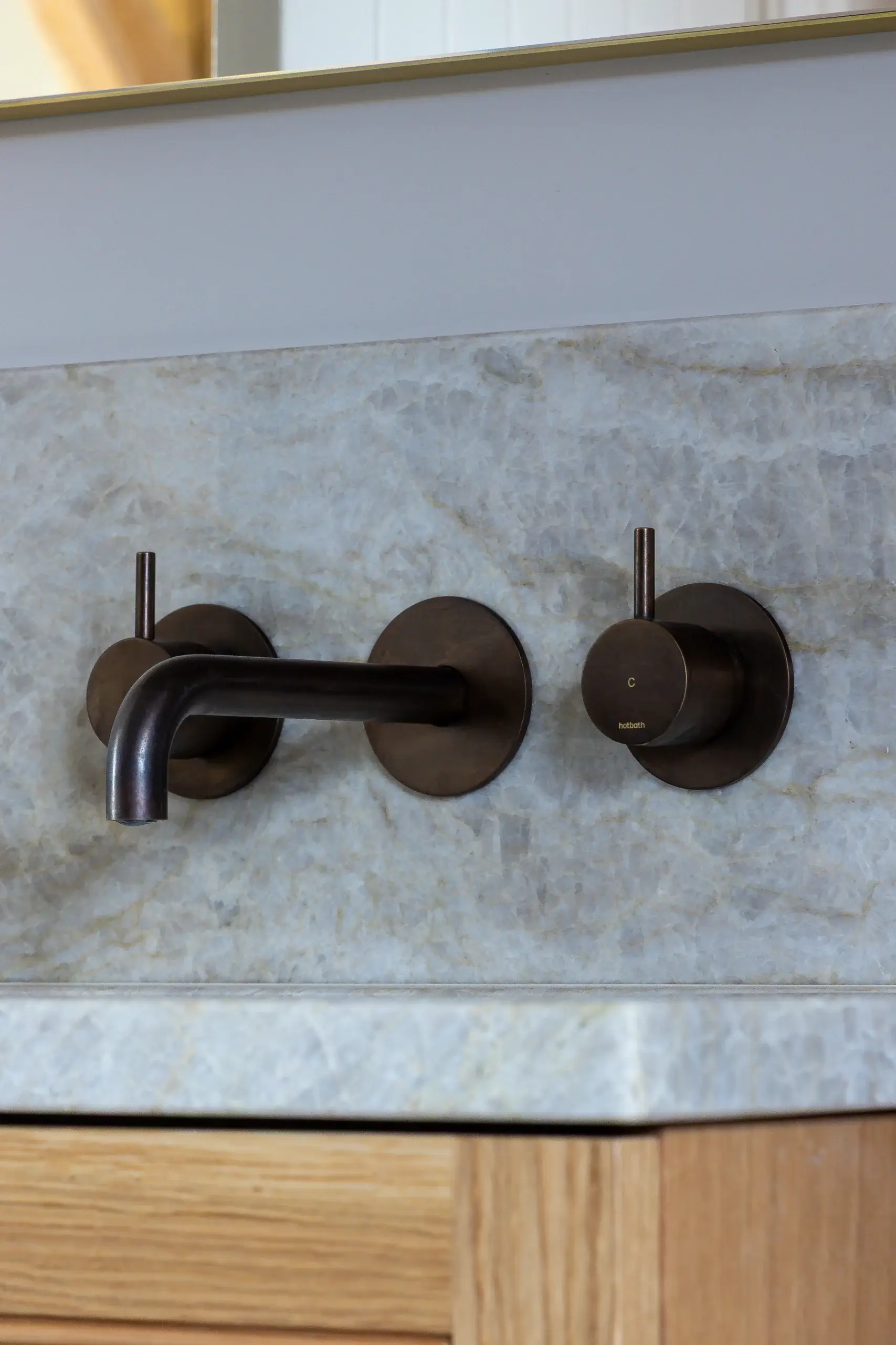 Wall-mounted oil-rubbed bronze faucet and separate hot/cold round handles set against a light gray marble backsplash.