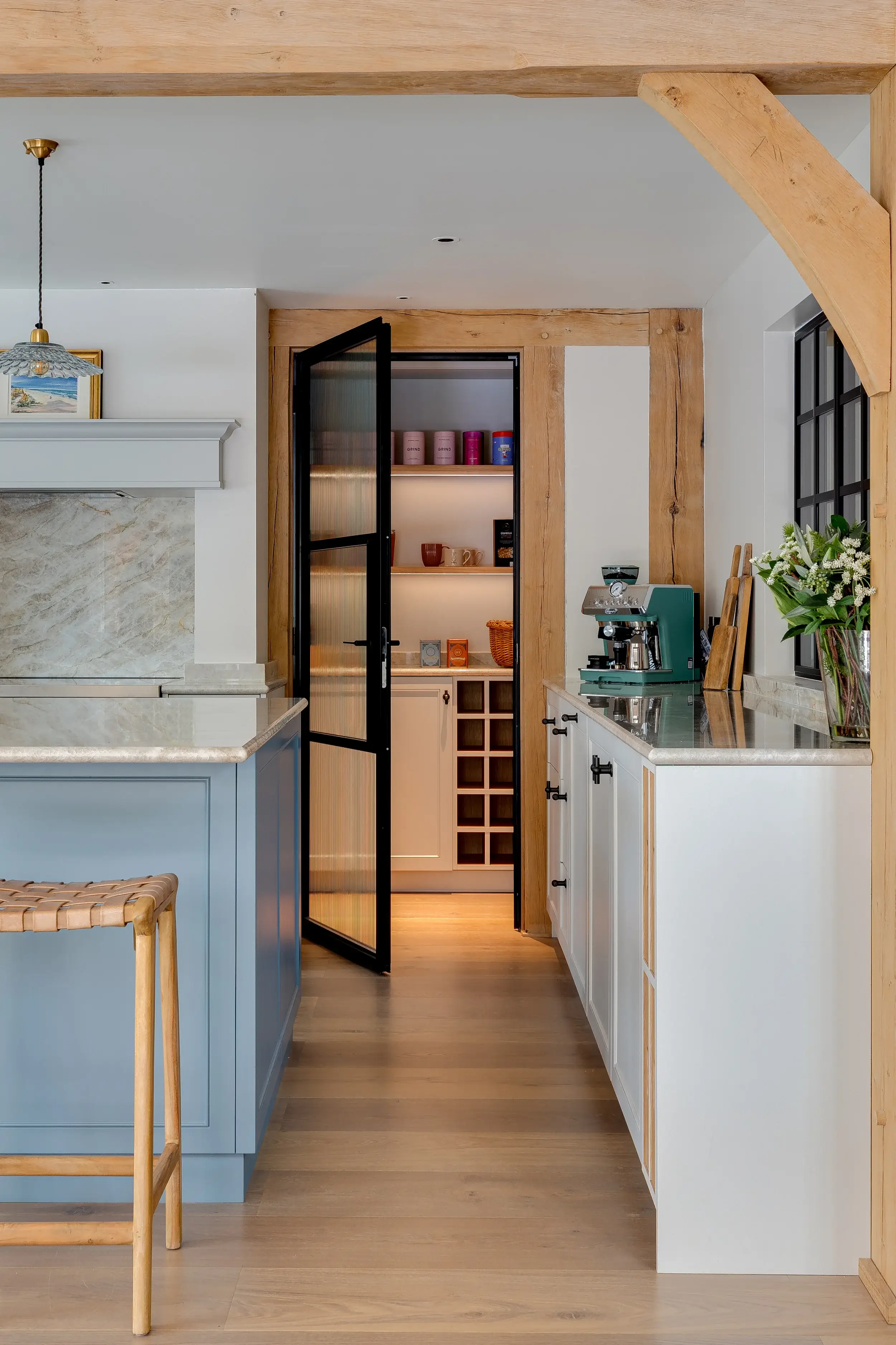 Elegant kitchen design with oak beams, painted cabinetry, and a view through to a walk-in pantry with open shelving.