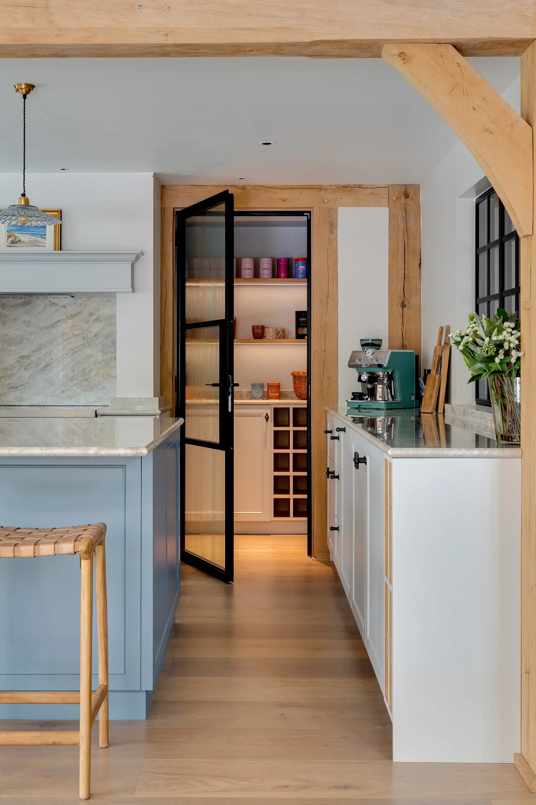 Bright modern kitchen with light wood beams, blue island, glass-paneled pantry door and teal espresso machine on white counters
