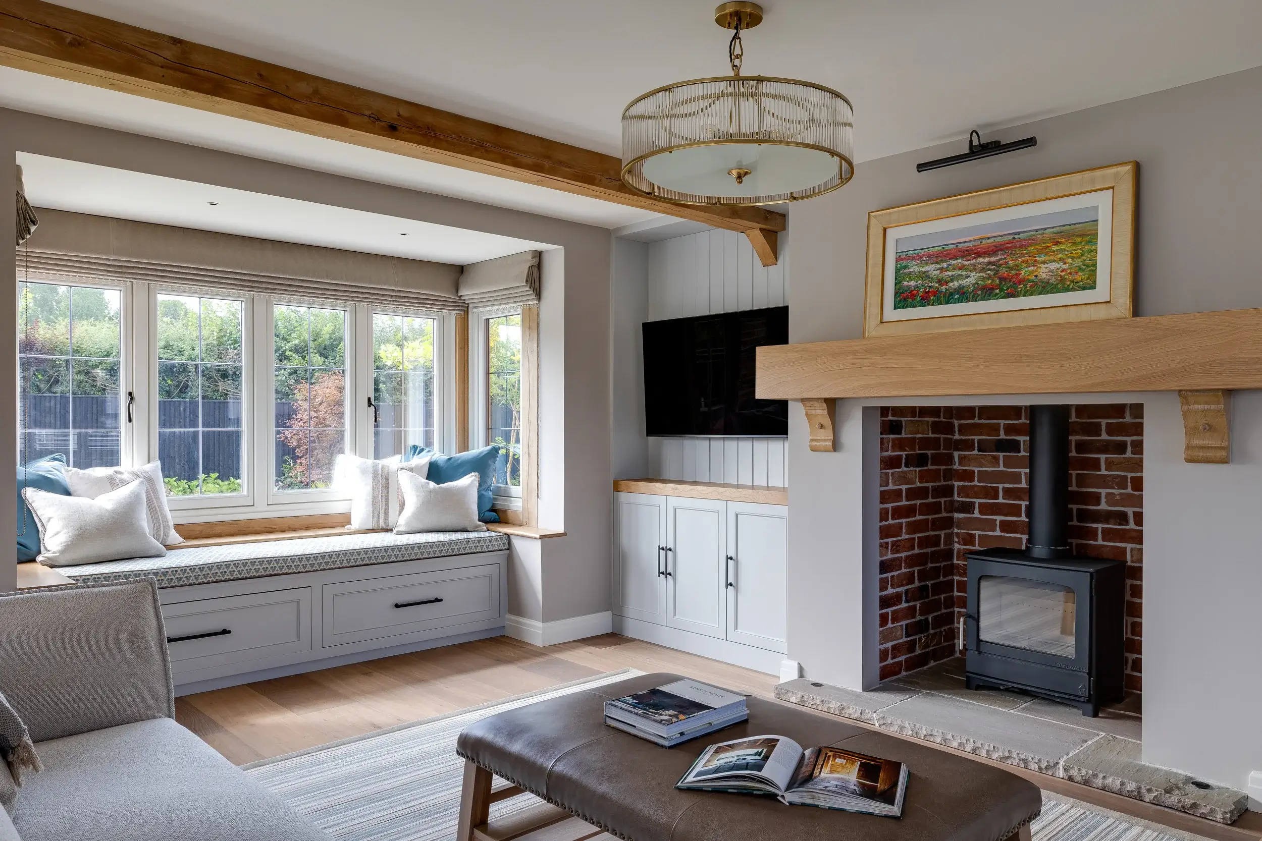 Bright living room with media wall, window seat with storage, and a brick fireplace framed by an oak mantel.