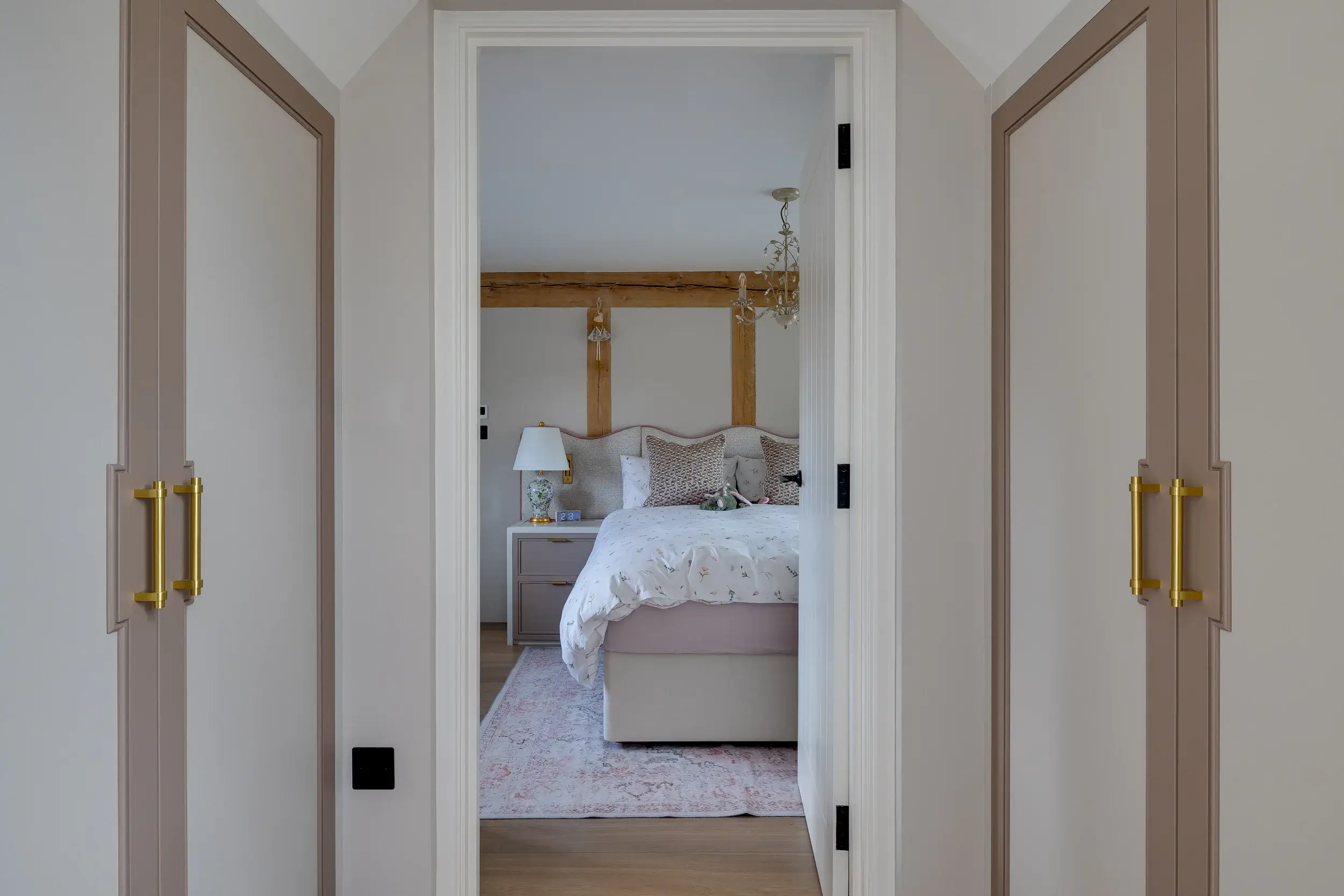 View through to a cosy bedroom, framed by bespoke wardrobes with muted pink panels and brass handles.