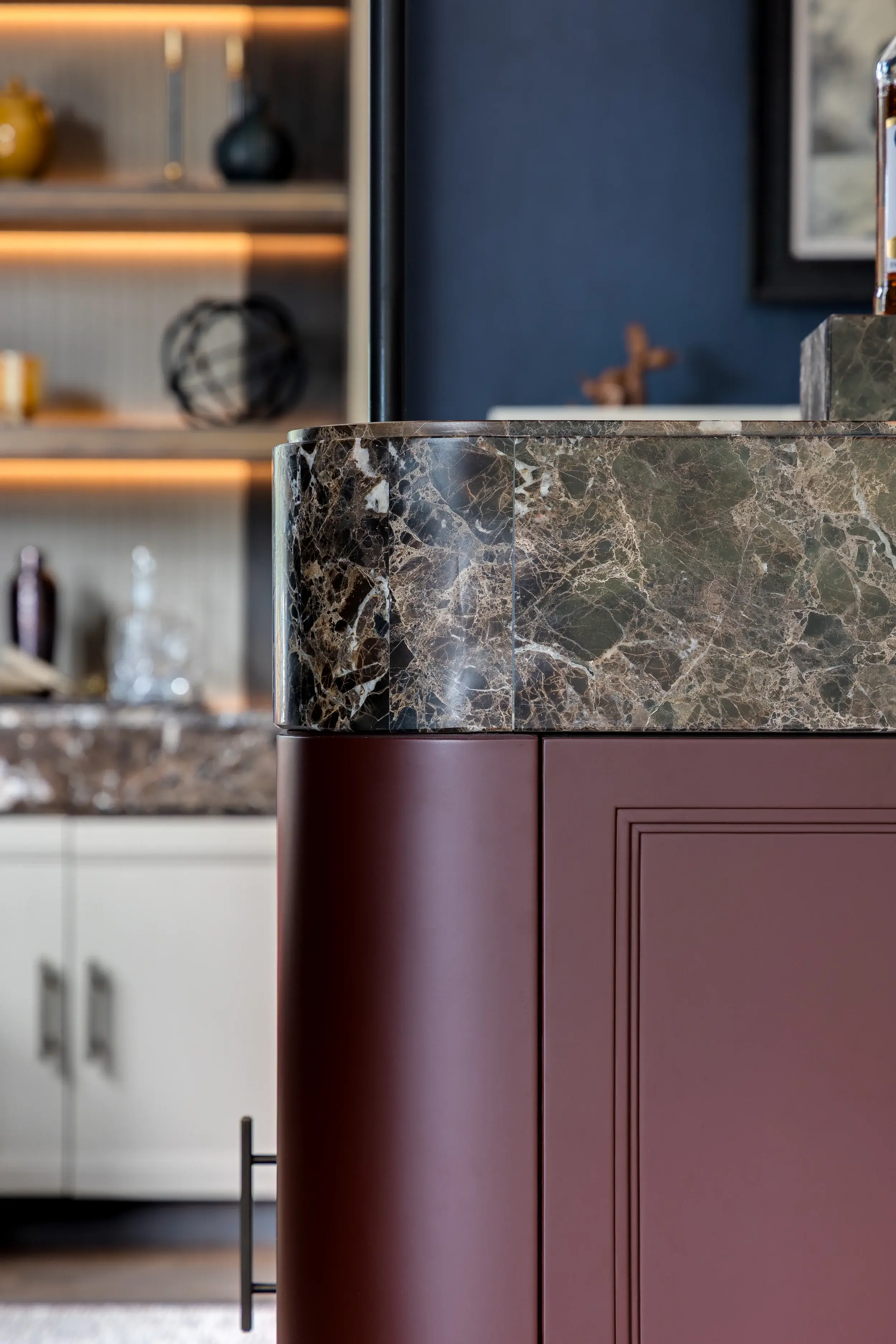 Close-up of a bar unit with a curved marble countertop and deep red cabinetry.