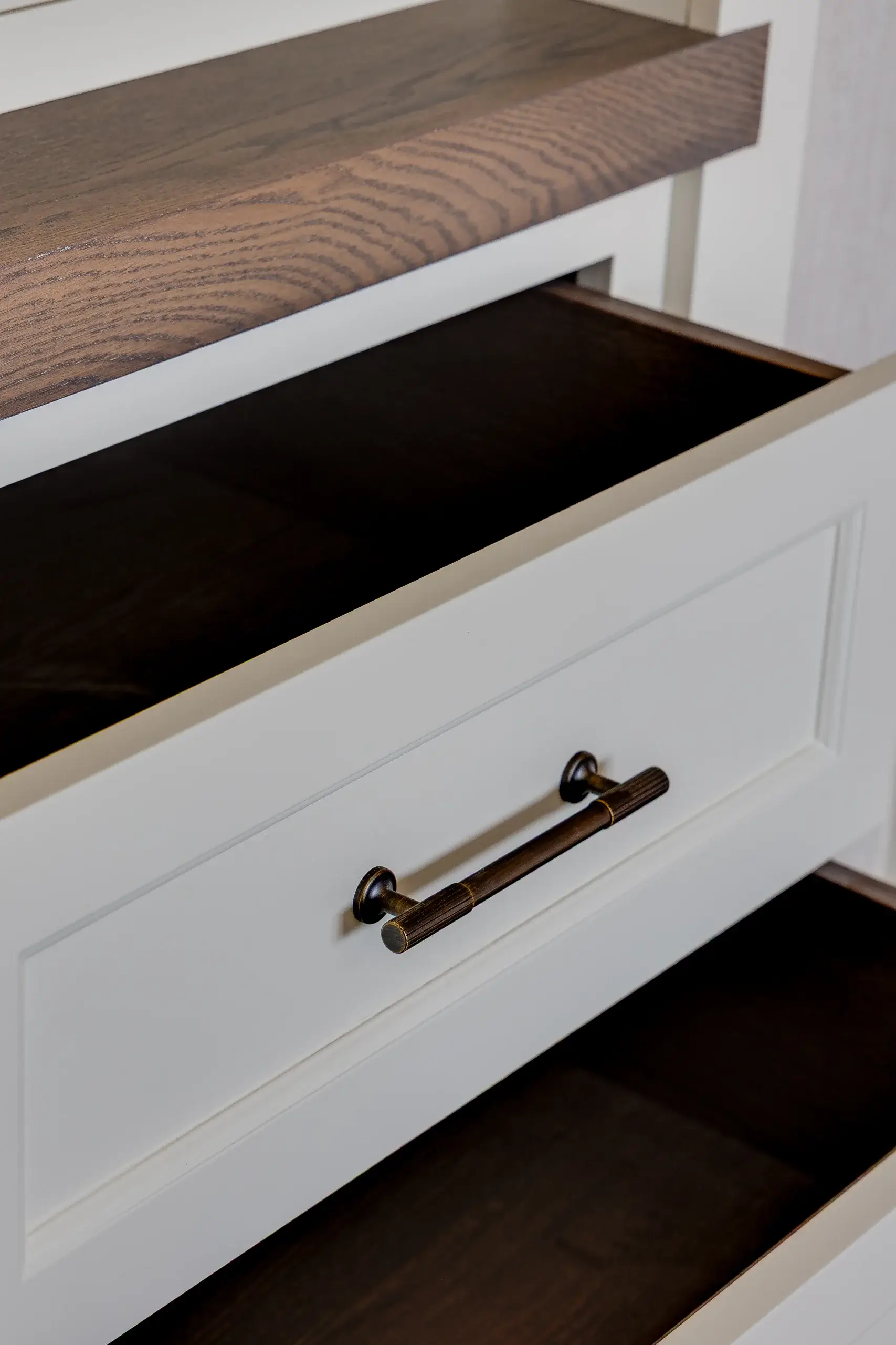 White dresser drawers with dark wood interiors and a brass cylindrical pull handle, topped by a wood shelf with visible grain.