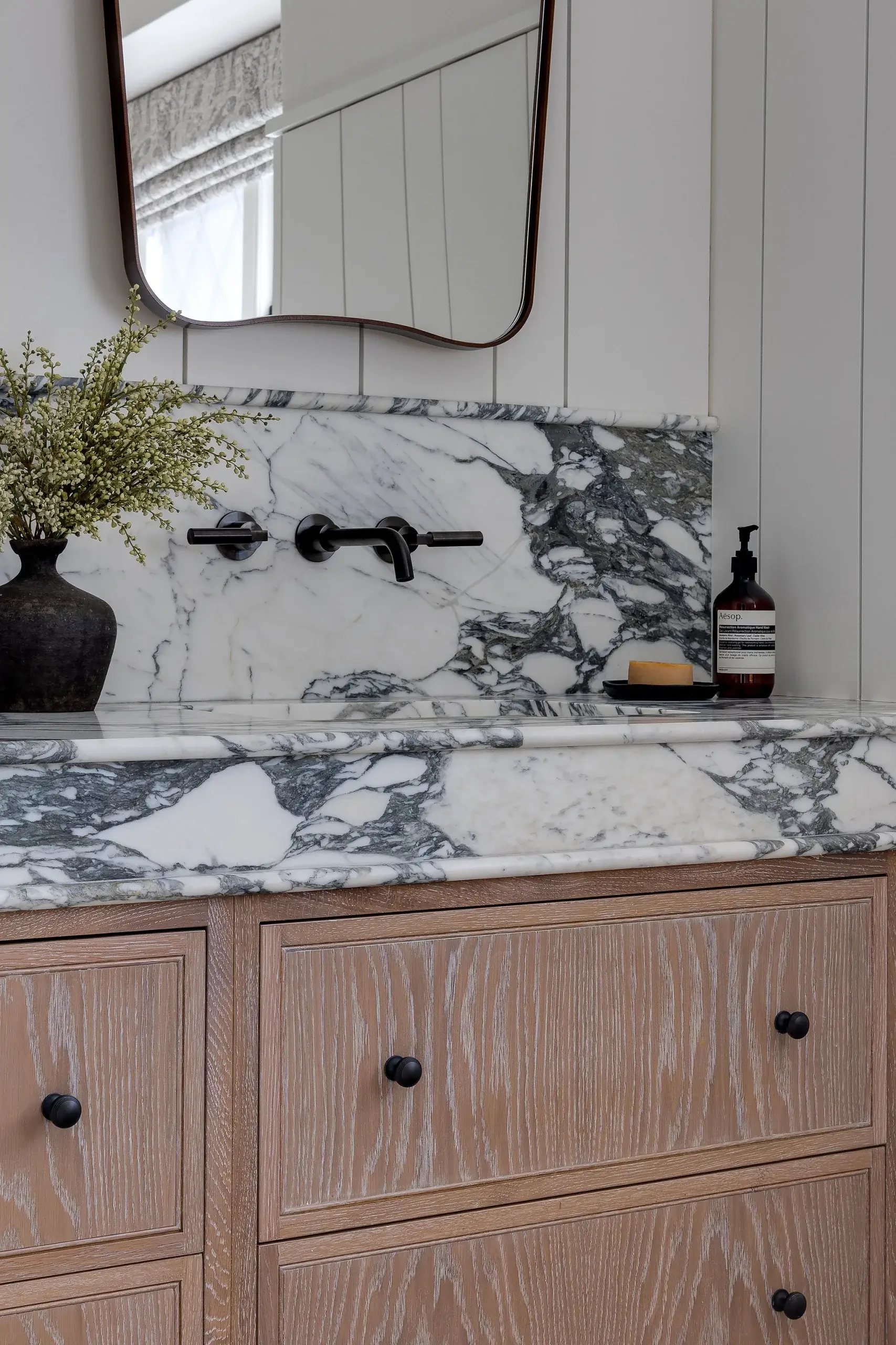 Oak vanity with marble worktop and splashback, featuring dark bronze fixtures and fine joinery detailing.