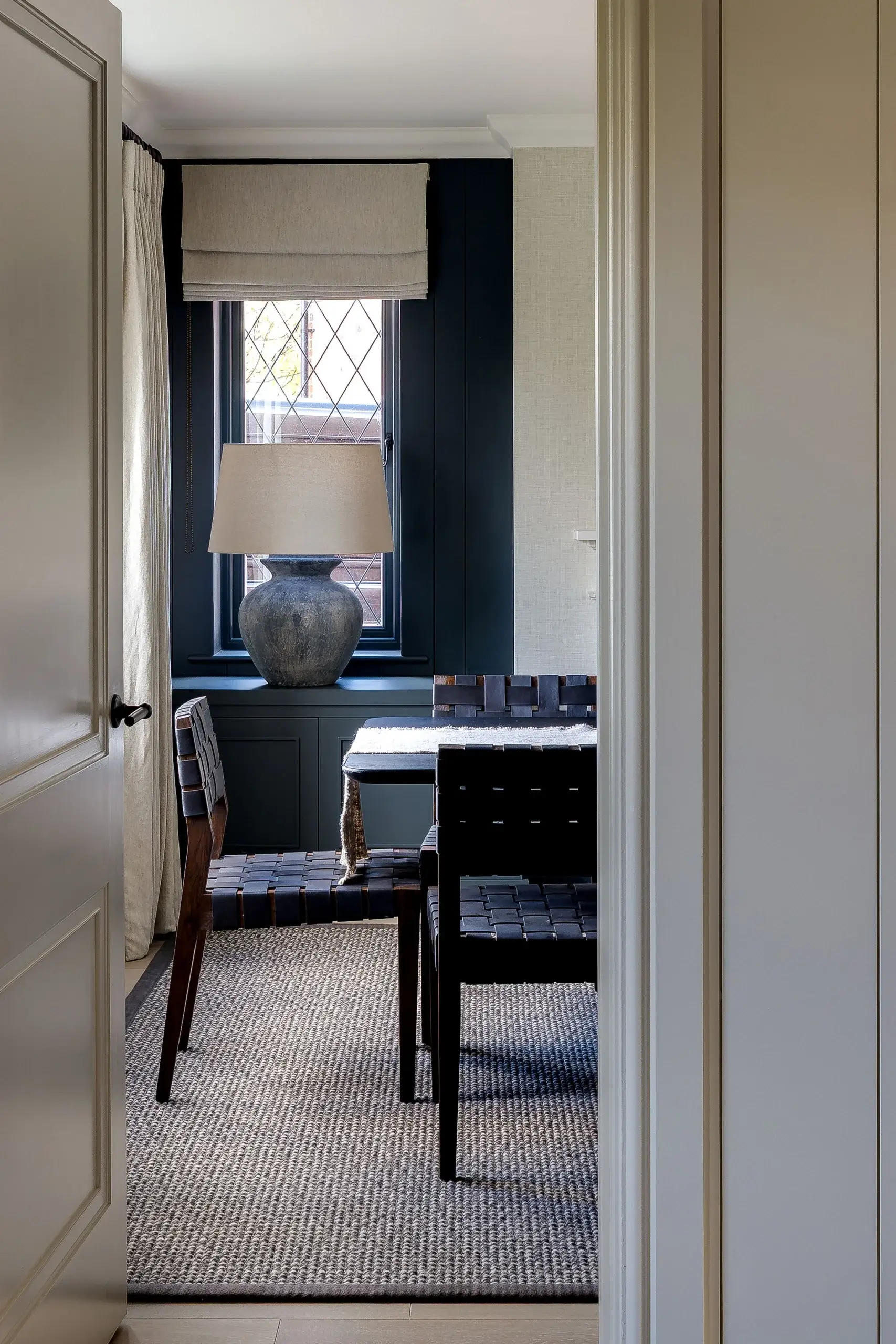 View into the dining room showing deep blue joinery, panelled walls, and a textured rug under woven leather chairs.