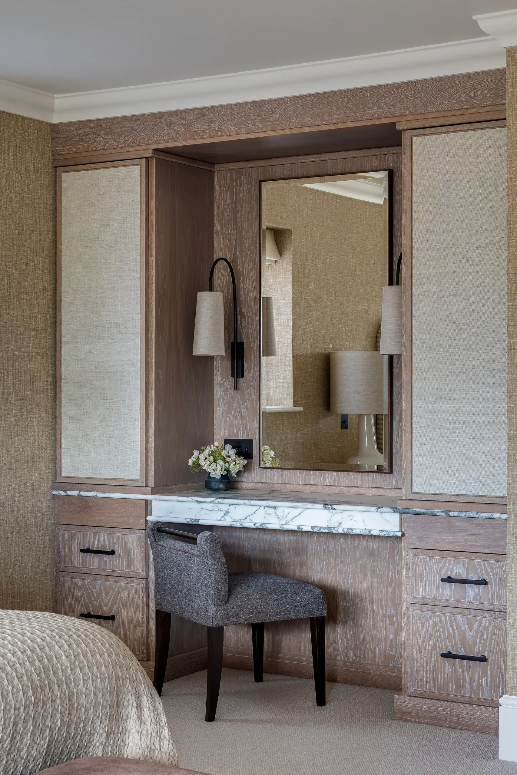Bespoke dressing table with marble top, oak cabinetry, integrated lighting, and upholstered chair in textured grey fabric.