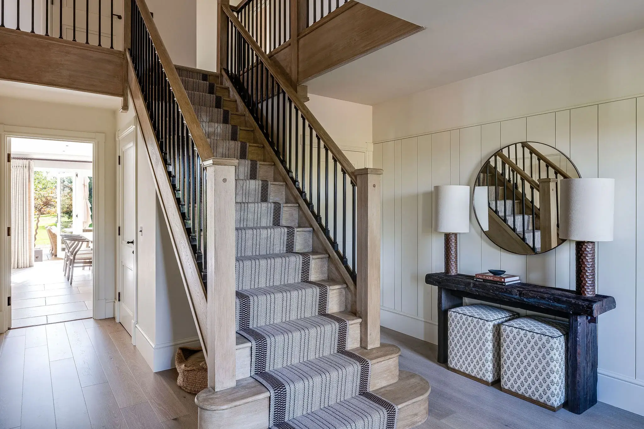 Oak staircase with black balustrades and striped runner, leading into a bright hallway with bespoke joinery.