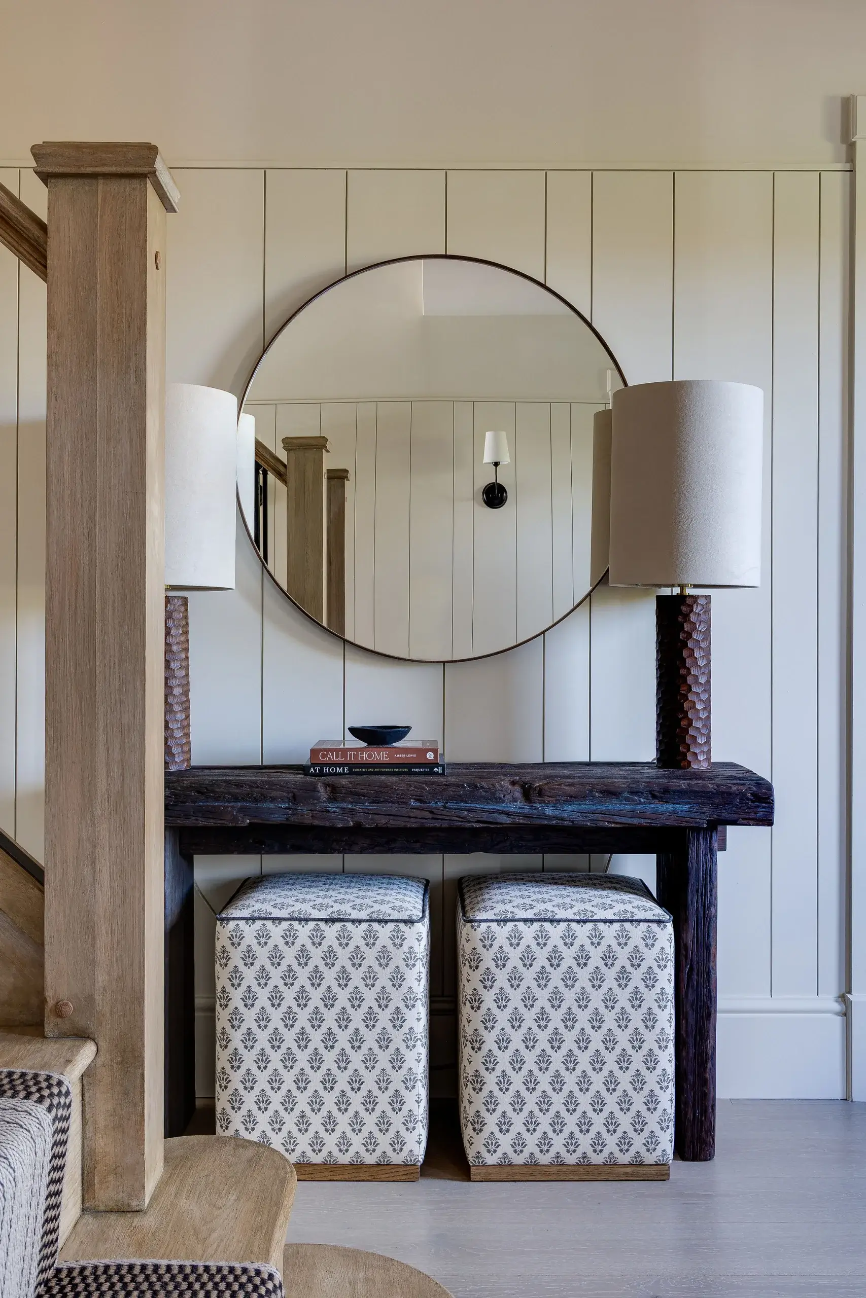 Entrance hallway with bespoke timber console table, round mirror, and linen-covered stools beneath.