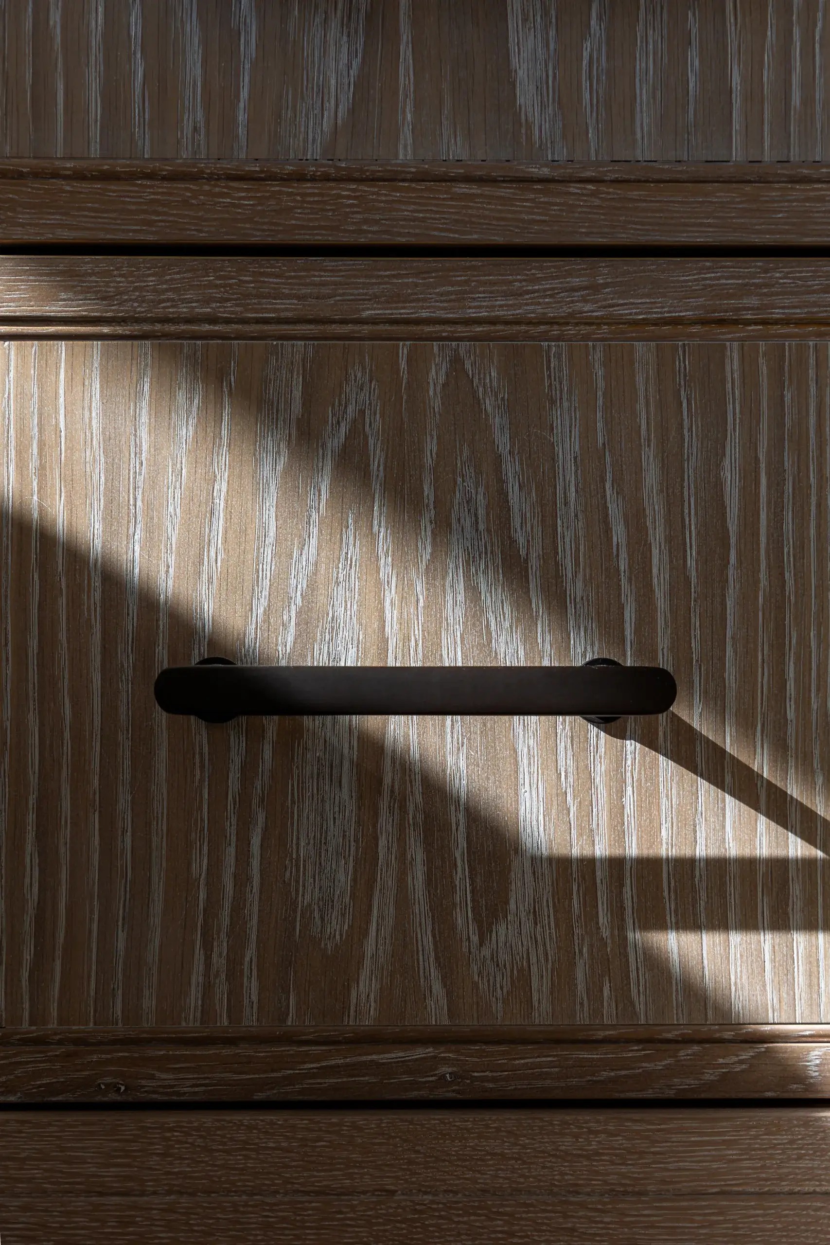 Close-up of black metal handle set against limed oak grain, showcasing refined texture and precision joinery.