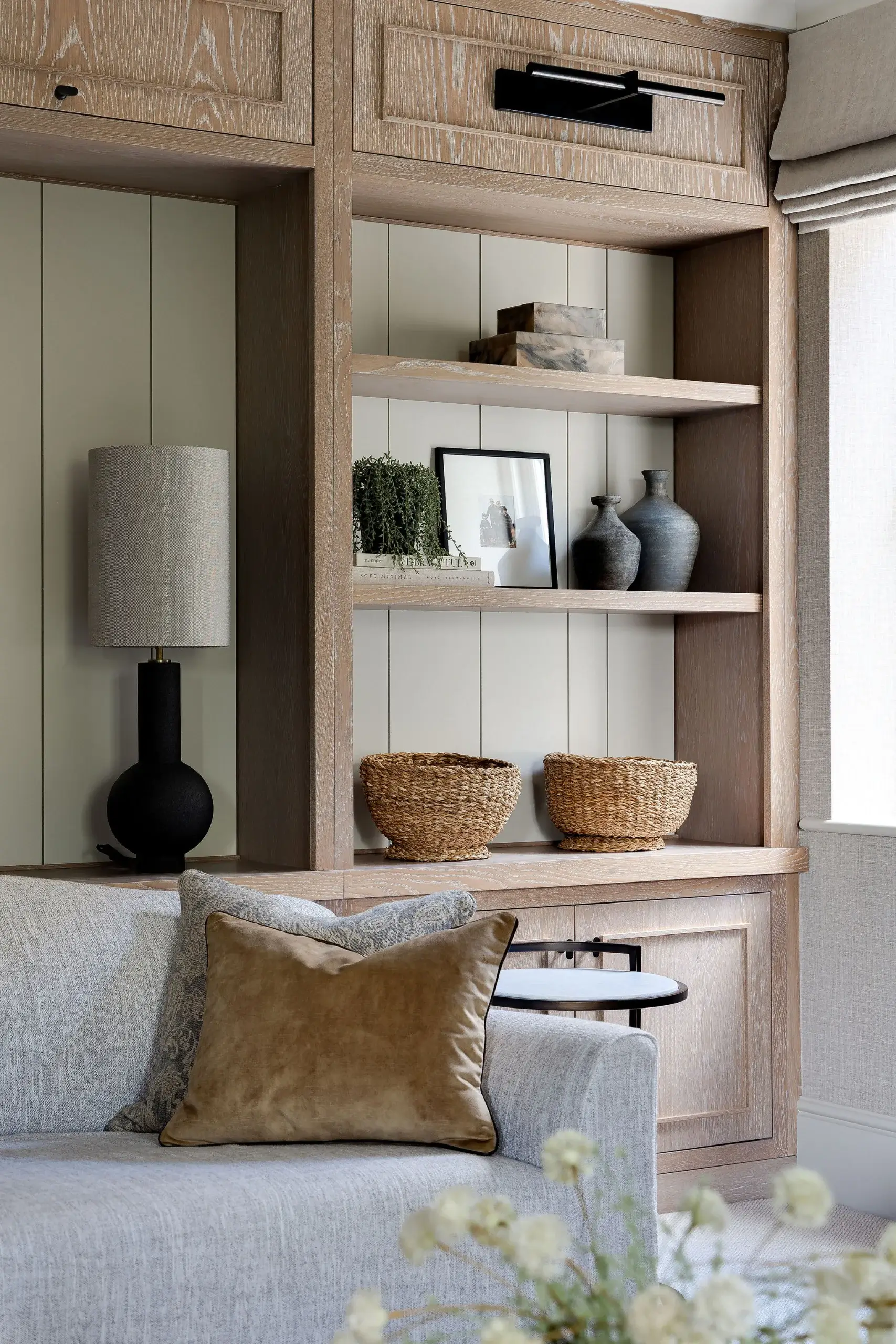 Bespoke oak shelving with integrated lighting, displaying woven baskets, ceramic vases, and framed artwork.