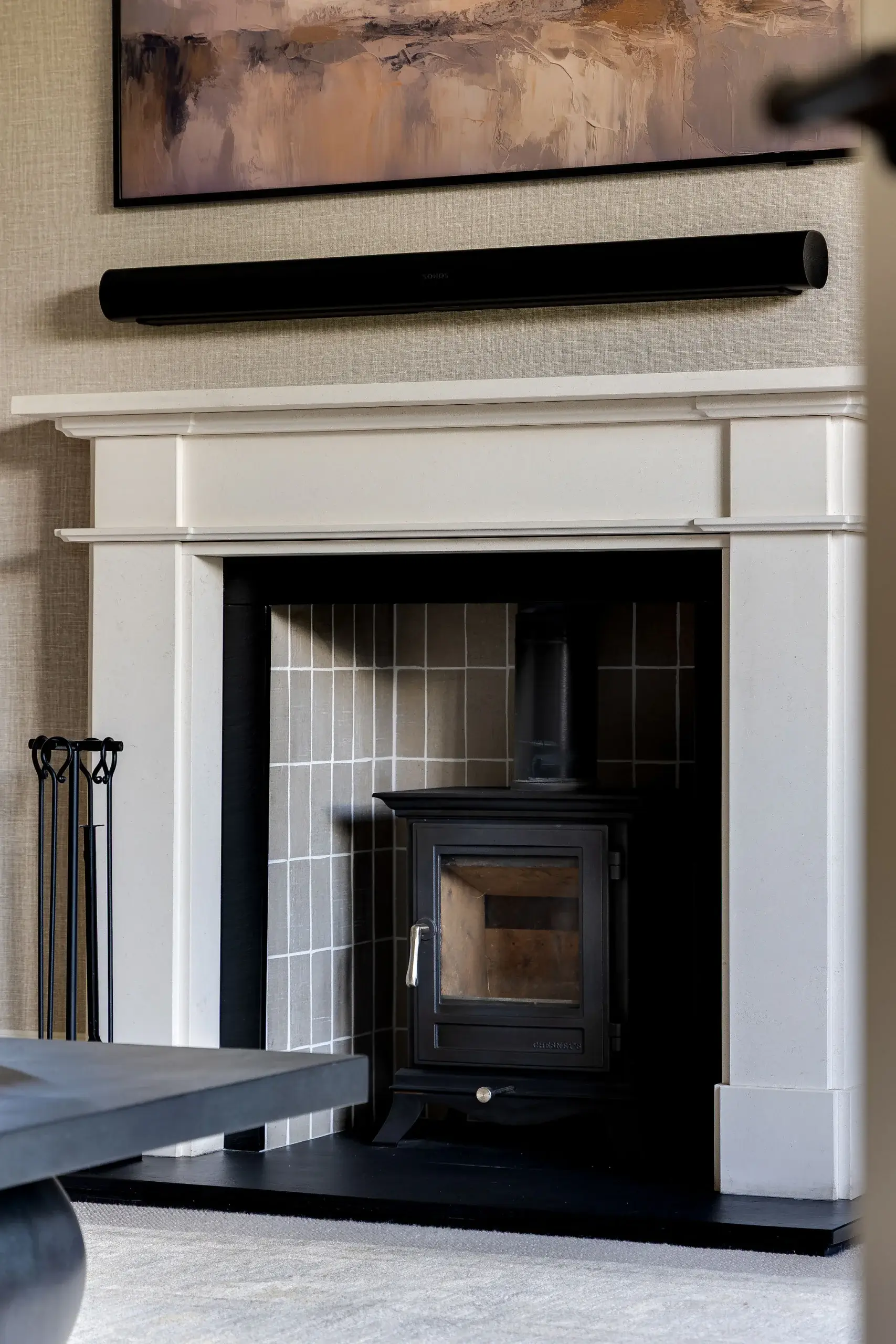 Close-up of the living room fireplace with a white surround, tiled inset, and black log burner beneath an abstract artwork.
