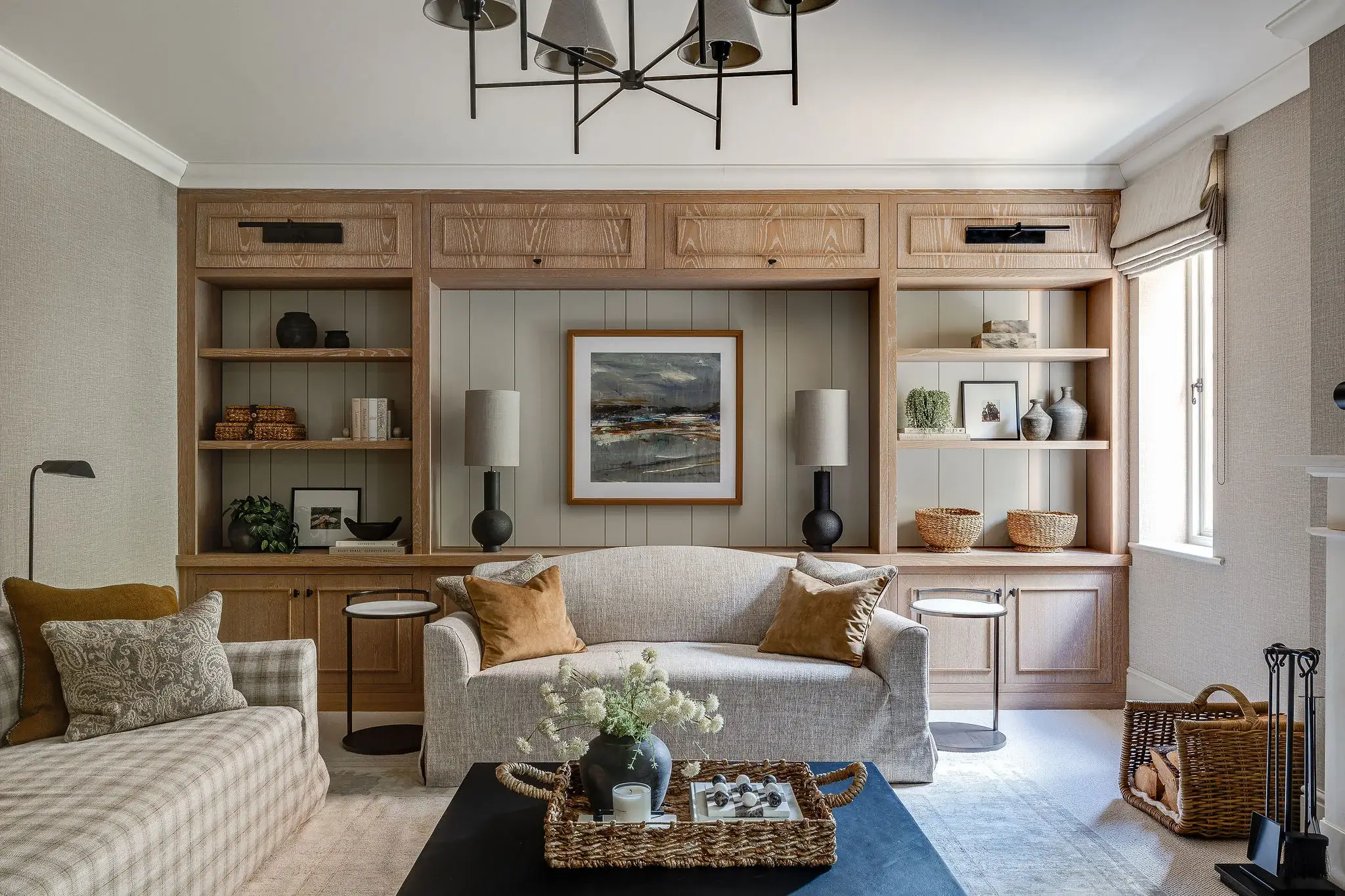 Symmetrical joinery framing the sofa, featuring oak shelving, wall lighting, and decorative storage detailing.