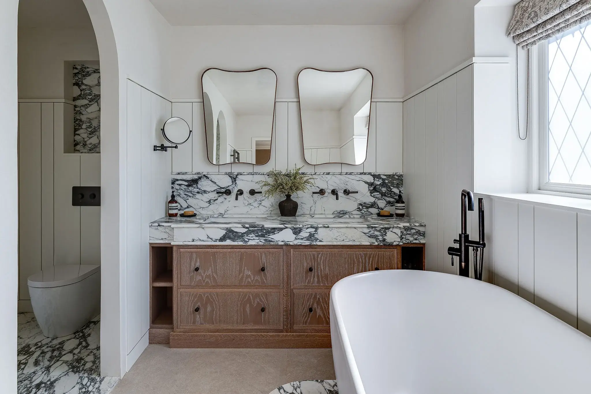 Double vanity in oak with striking marble top and splashback, paired with brushed bronze fittings and twin mirrors.
