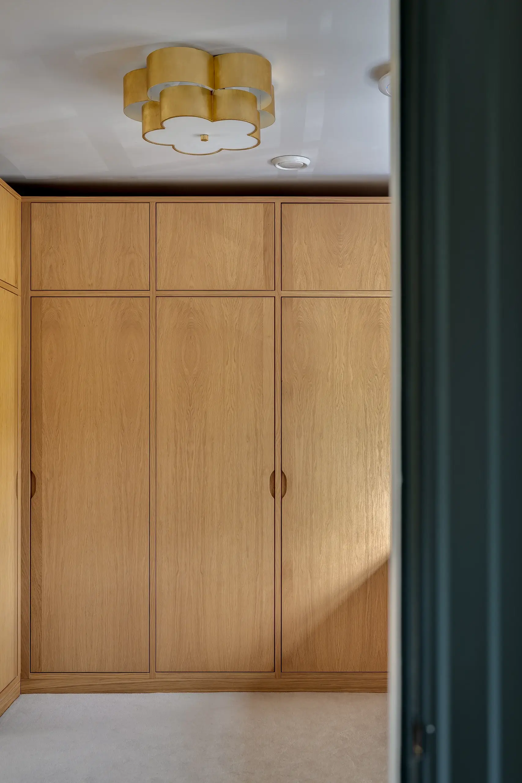 Built-in floor-to-ceiling oak wardrobes with minimalist recessed handles and a clover-shaped brass ceiling light above.