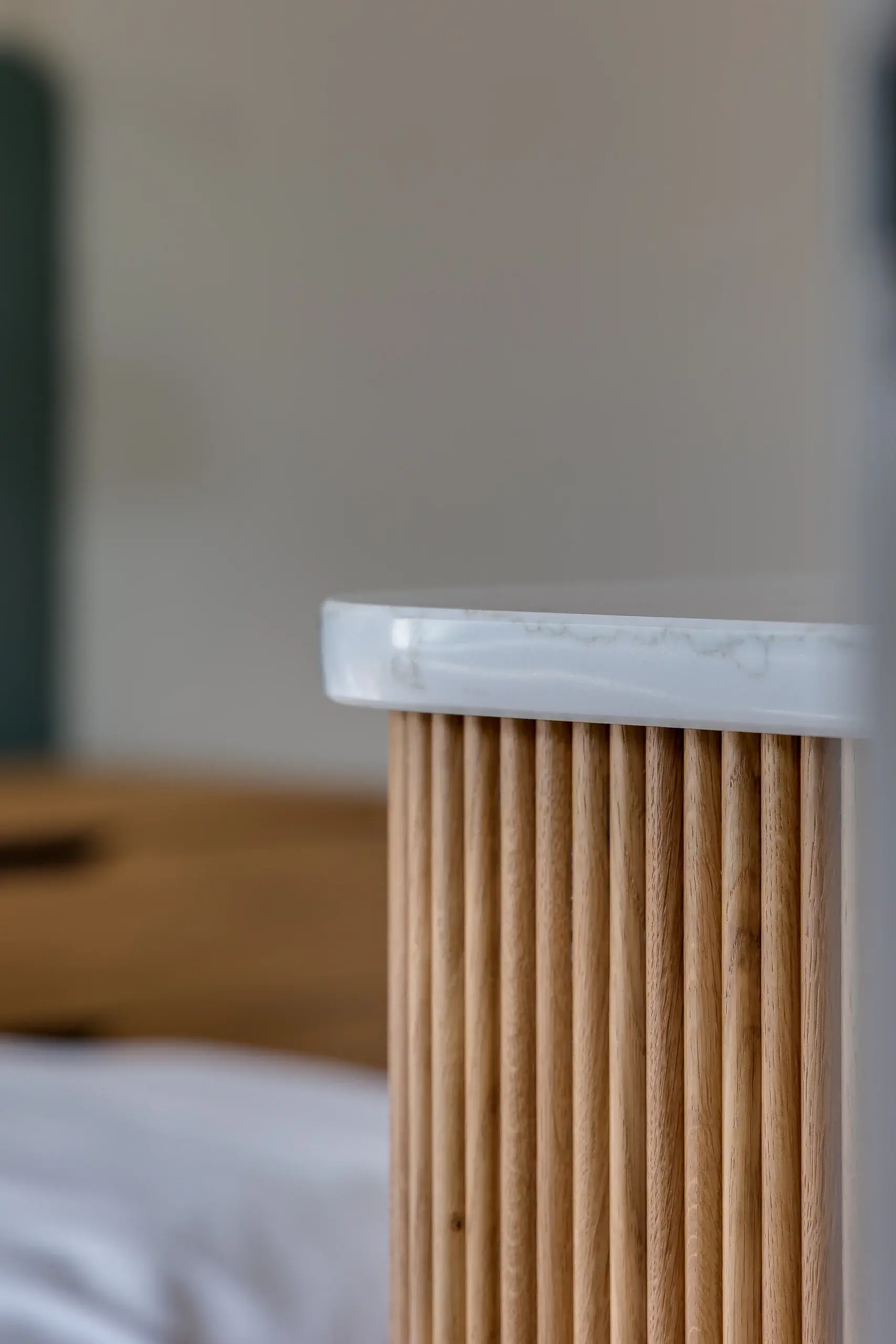 Close-up of a white marble tabletop edge above vertical fluted light wood slats, blurred neutral background.