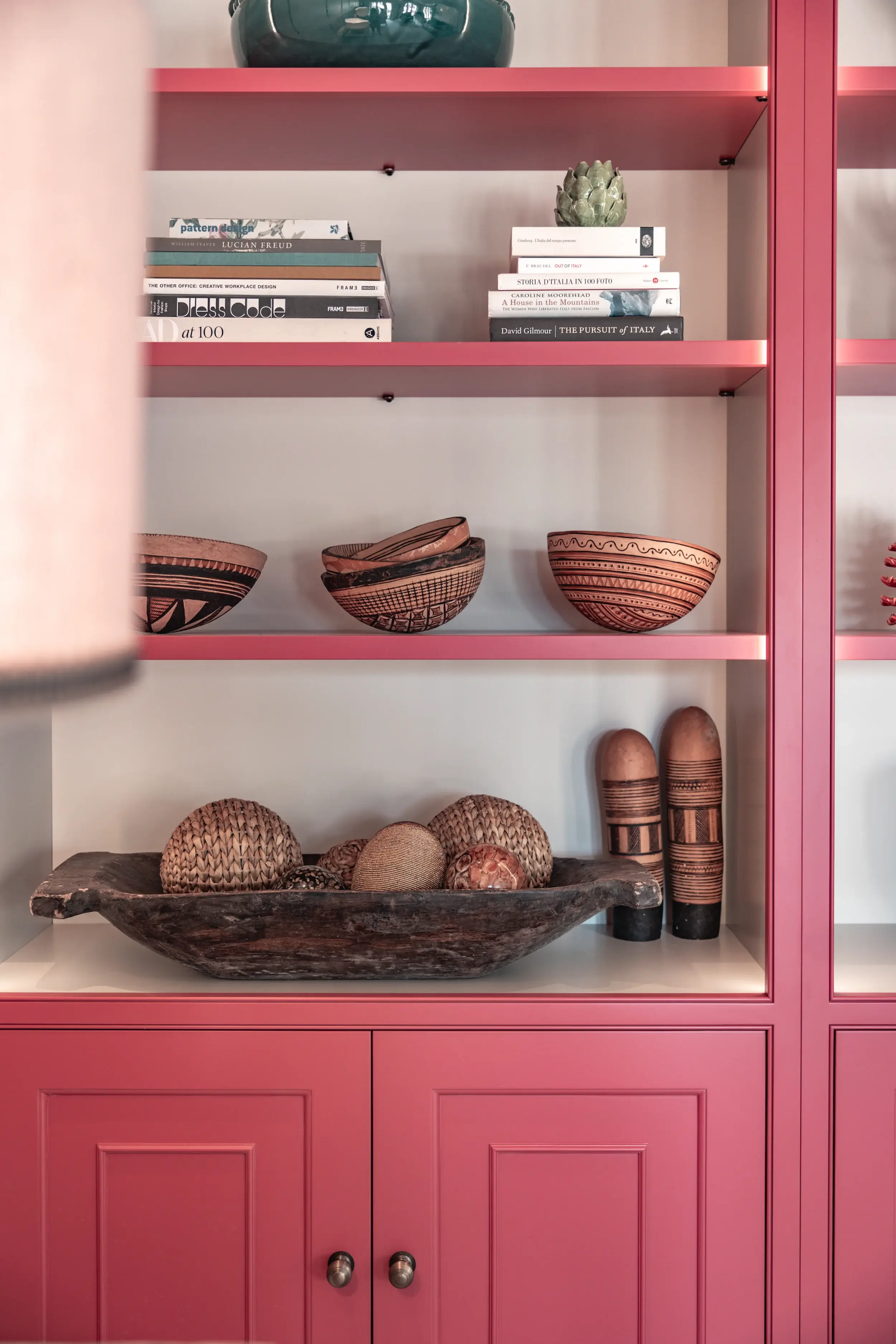 Raspberry-painted bookcase with integrated display shelving and decorative tribal bowls