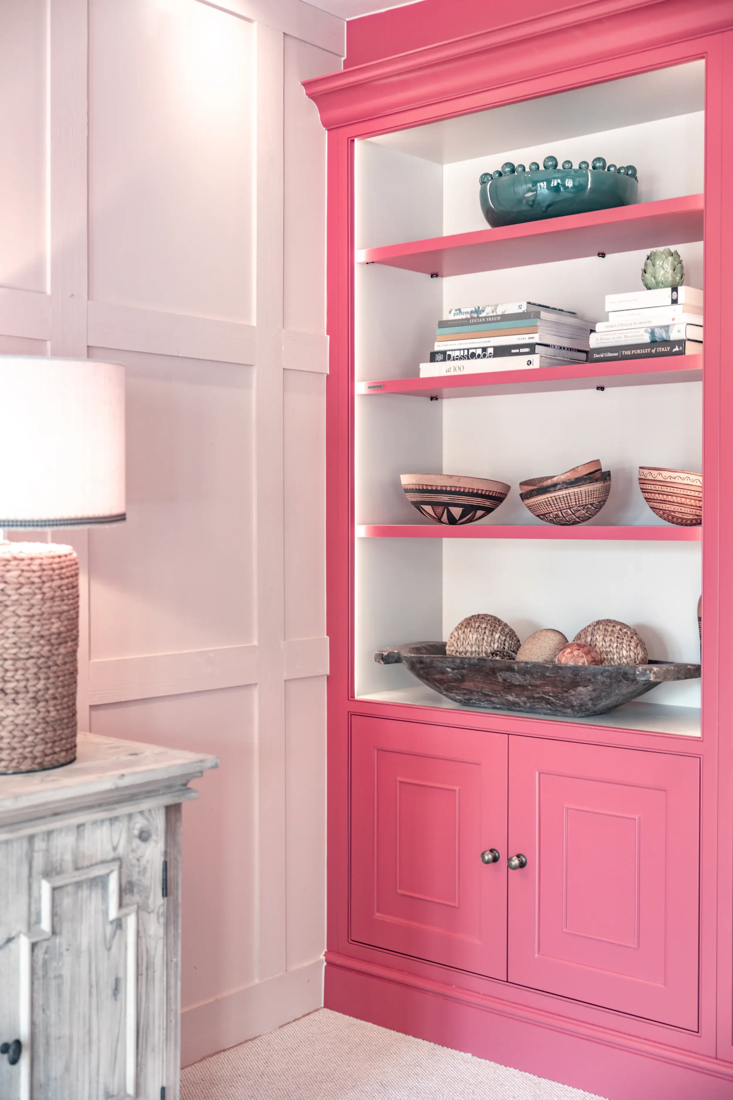 Bold pink custom-painted bookcase with open display shelves and shaker-style lower cabinetry